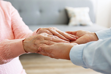 Mature female in elderly care facility gets help from hospital personnel nurse. Senior woman w/ aged wrinkled skin & care giver, hands close up. Grand mother everyday life. Background, copy space.