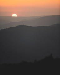 Amazing background of orange sunset behind silhouettes of rows of hills