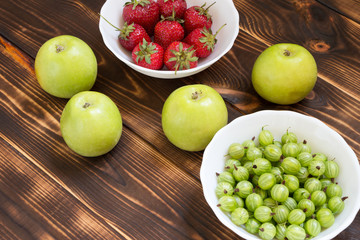 Naklejka na ściany i meble Summer fruits and berries background. Green whole juicy apples, gooseberries and strawberries in white bowls on rustic wooden table.