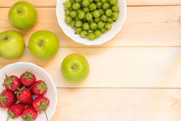Summer harvest of fruits and berries background with copy space. Green whole juicy apples, gooseberries and strawberries in white bowls.