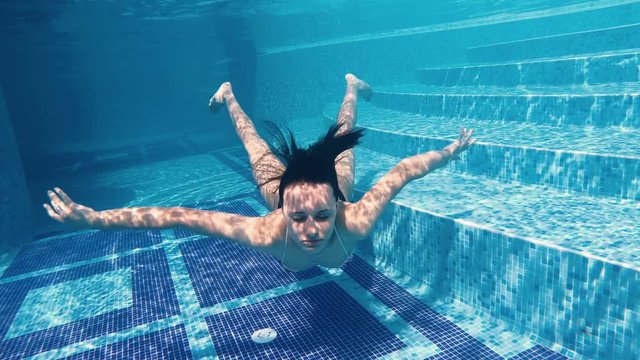 Happy teen girl swimming underwater in luxury pool smiling