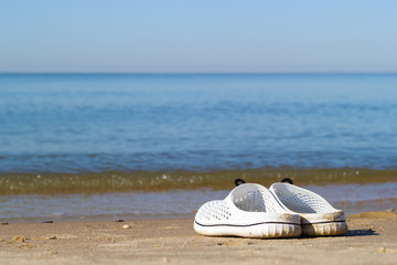Close-up of white sea slippers on the golden sand near the sea water. Holidays at sea background with copy space.
