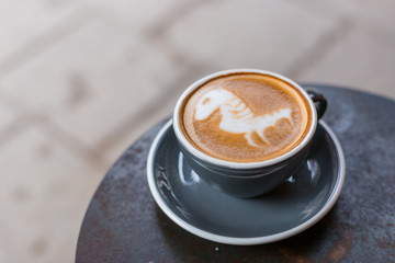 Gray cup of cappuccino with latte art on the table in cafe. Tasty cappuccino with horse latte. Top view.