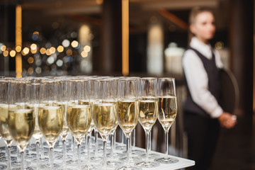 Glasses with champagne at buffet and waiter on background.