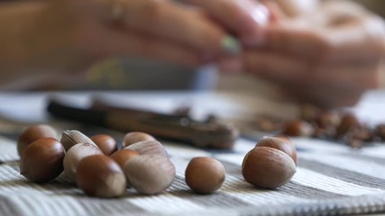 Close-up of the hands of a girl who sits at a table and cleans a filbert. Tasty, healthy nuts