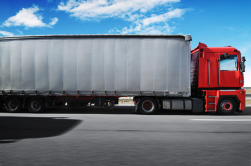 Truck with a trailer driving fast on the countryside road against sky with clouds
