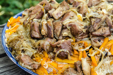 Oriental cuisine: pilaf with lamb on a national dish on a wooden table