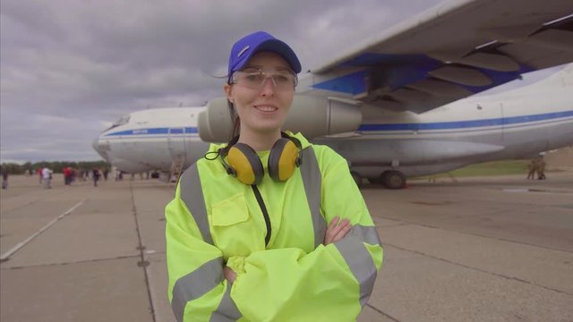 woman airport worker on the background of the aircraft posing crossing his hands smiling and looking at the camera