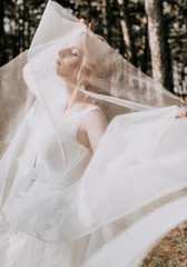 Fototapeta na wymiar Beautiful blonde bride with stylish make-up in white dress in the garden