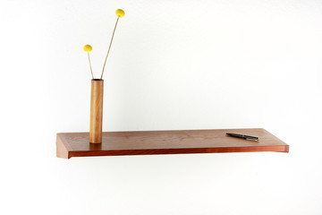 midcentury teak shelf on white wall in the living room with a wooden vase and a plack pen on it...