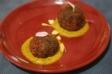 Squid ink Arancini, breadcrumb coated rice balls with squid ink served on the ceramic red plate