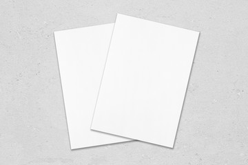 Two empty white poster mockups lying diagonally on top of each other on grey concrete background