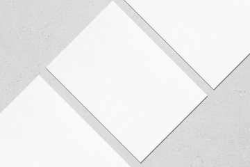 Closeup of three empty white rectangle poster mockups lying diagonally with soft shadow on neutral light grey concrete background. Flat lay, top view. Open composition.