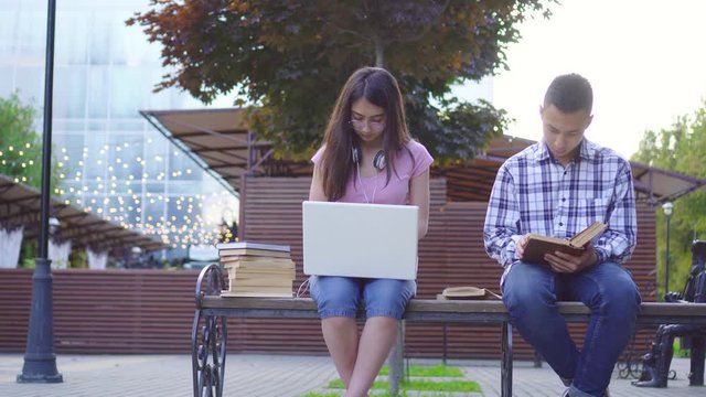Young asian students man with a book and a woman with a laptop sitting on a bench