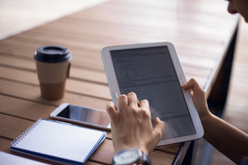 Women's hands with neat manicure and large wristwatch, work with gadgets, tablet, smartphone, papers on a wooden table.