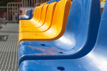 Rows of empty blue and yellow plastic chairs in bright sunlight. Urban architecture 
