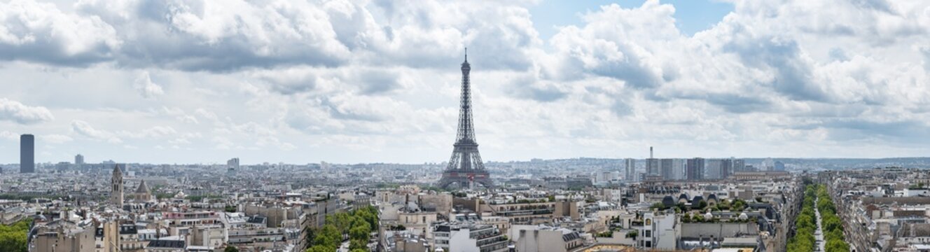 Large panoramic cityscape of Paris, France, with the Eiffel Tower centred in the image under a dramatic cloudy sky.