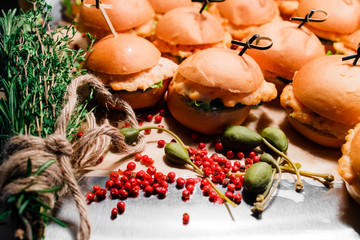 homemade burgers lie on a table decorated with rosemary, red pepper and capers