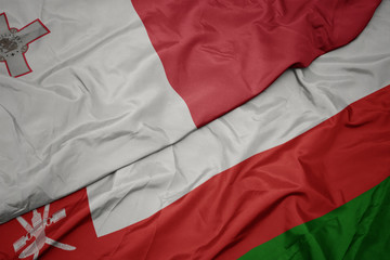 waving colorful flag of oman and national flag of malta.