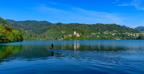 Fototapeta na wymiar Landscape with Bled Island, in the foreground a man and a dog on a swimming board.