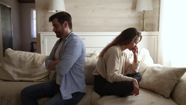 Unhappy couple ignoring each other sitting apart on couch