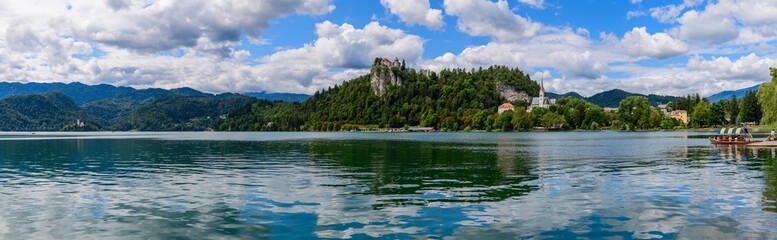 Fototapeta na wymiar Beautiful panoramic view mountain lake Bled with Castle in the foreground, the Catholic Church and a small island with Pilgrimage Church of the Assumption of Maria and Bled Castle in background. .