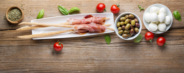 Prosciutto and grissini with cherry tomatoes, Taggiasca olives and small mozzarella. Italian appetizer.