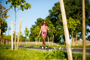 Teenager. Young pretty sporty caucasian girl in a pink jumpsuit and sunglasses in the park on a sunny day in summer.