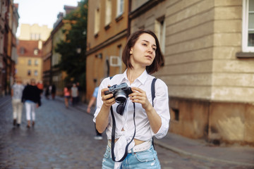 The girl in the black hat and sun glasses with photo camera on a road in an old european town.