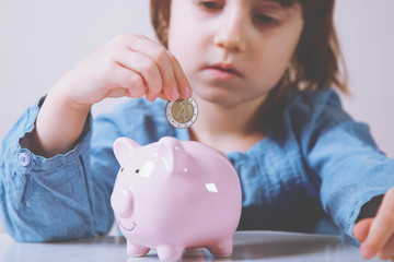 Portrait of little cute child girl putting money in piggy bank for saving. Investments concept.