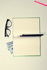 glasses on a clean notebook pages on white table background pink red blue black white color pencils dollars money
