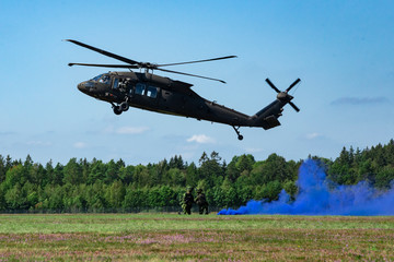 Fototapeta na wymiar Landing of swedish military helicopter Blackhawk UH-60 on airshow at Ronneby flygdag Military armed men with smoke bomb