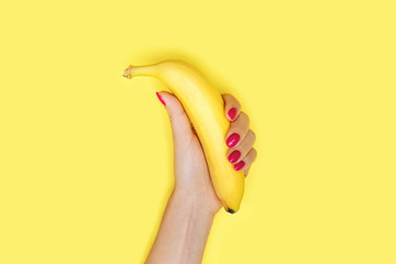 Yellow banana in women's hand with trendy manicure on yellow background.