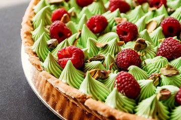 Tart with raspberries and pistachios green cream. Menu for cafe, restaurant, cake black background. Macro, details.