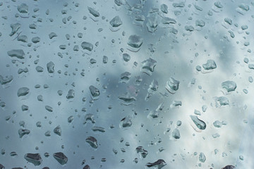Drops of water after rain on a glass surface reflect the sky with clouds