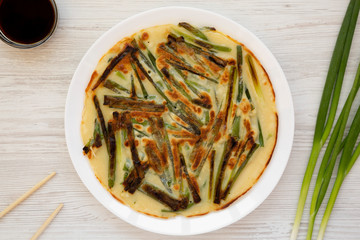 Homemade korean Pajeon scallion pancake on a white plate on a white wooden surface, top view. Asian food. Flat lay, overhead, overhead.