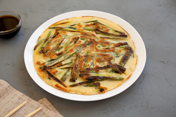 Homemade korean Pajeon scallion pancake on a white plate on a gray background, side view. Asian food.