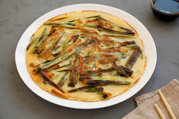 Homemade korean Pajeon scallion pancake on a white plate on a gray surface, side view. Asian food. Close-up.