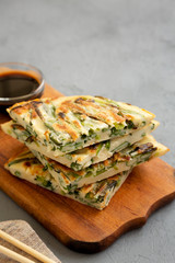 Homemade korean Pajeon scallion pancakes with soy sauce on a rustic wooden board on a gray surface, side view. Asian food. Copy space.