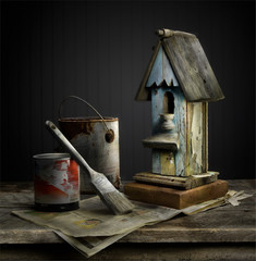Still life composed of old bird house, paint cans, and paint brush