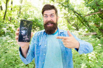 look here. happy bearded man pointing finger on phone. Mature hipster with beard. got lost in...