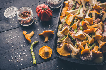 Close-up chanterelles and asparagus in a cast-iron baking dish on a dark wooden table.