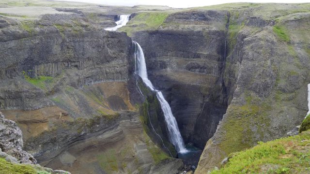 Granni, a thin very tall waterfall in Iceland. Very beautiful and dangerous. High canyon, cliffs and a river above. Green moss, stone and rocks. Overcast day.