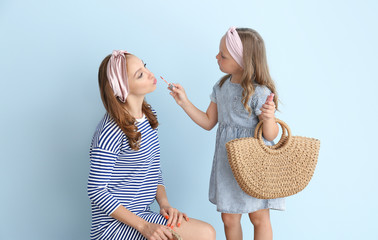 Little girl applying makeup on her mother's face against color background
