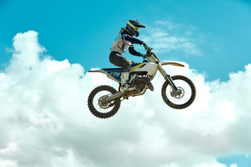 Fototapeta na wymiar Racer on motorcycle dirtbike motocross cross-country in flight, jumps and takes off on springboard against sky. Concept active extreme rest.