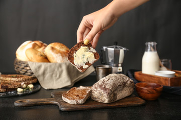 Woman taking slice of fresh bread with butter from table