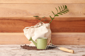 Eco bag with gardening supplies, soil and plant on wooden background