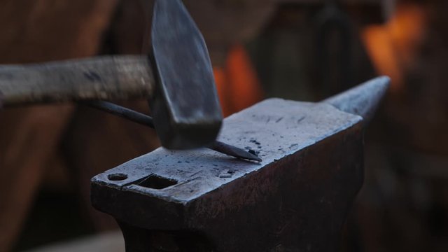 Blacksmith father and son forge hot steel on an anvil by hammer. Making arrowhead for bow.