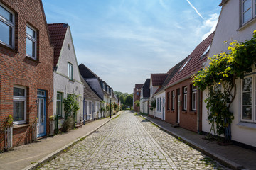 Fototapeta na wymiar street with low houses, cobblestones and roses in Friedrichstadt, the beautiful town and travel destination in northern Germany founded by Dutch settlers, copy space