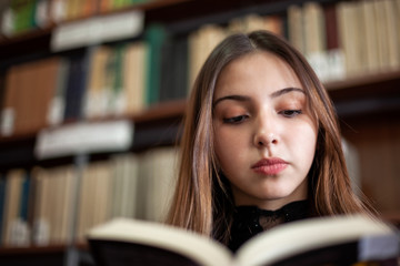 Beautiful teenager schoolgirl reading a book in the library